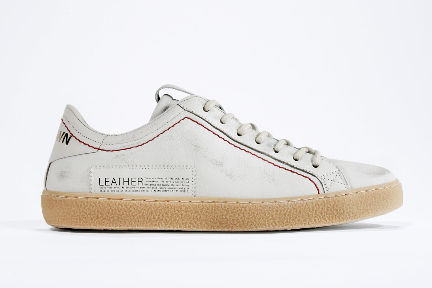 Side profile of low top white sneaker. Distressed white leather upper with red stitching and natural rubber sole.