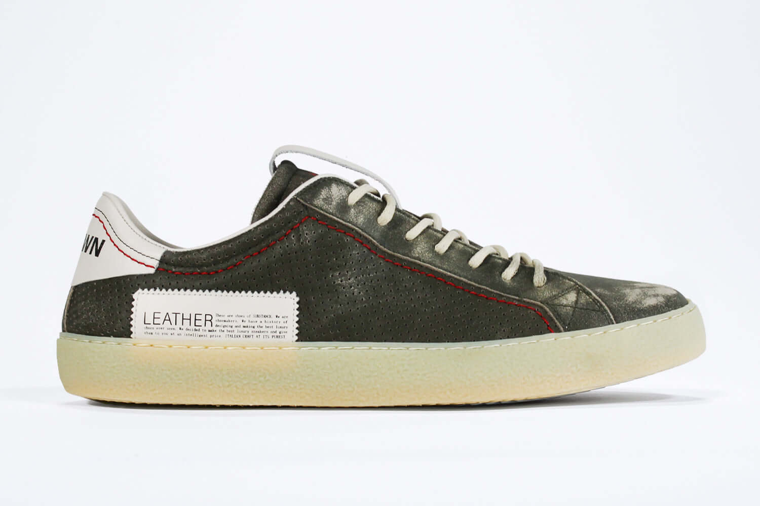 Side profile of low top aged khaki sneaker with white accents. Perforated khaki leather upper with red stitching and pale natural rubber sole.