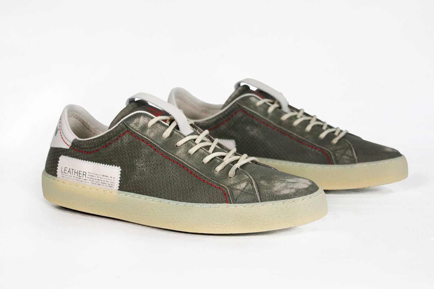Three quarter front view of low top aged khaki sneaker with white accents. Perforated khaki leather upper with red stitching and pale natural rubber sole.
