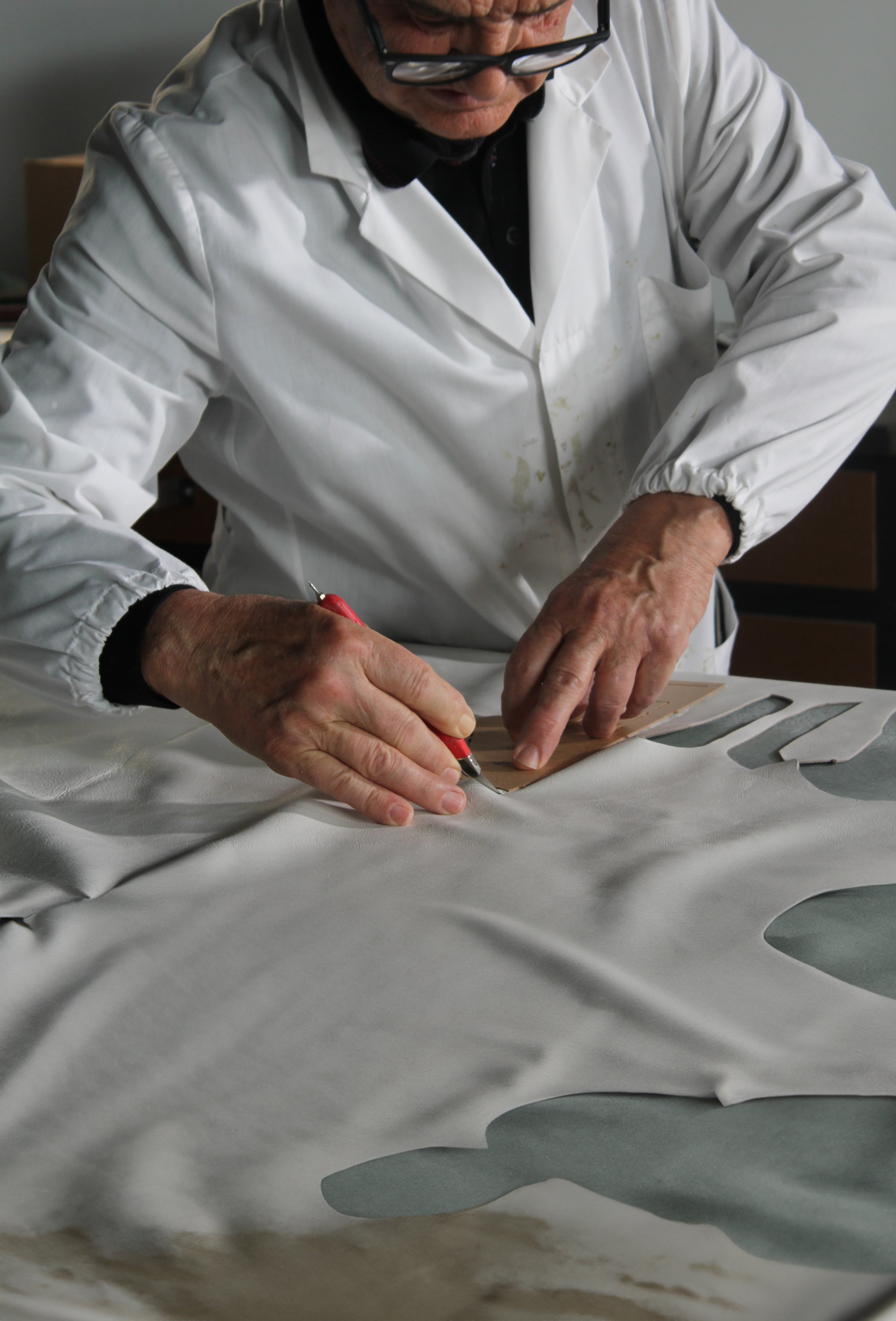 Artisan cutting pieces of leather for a Leather C|R|OWN sneaker.