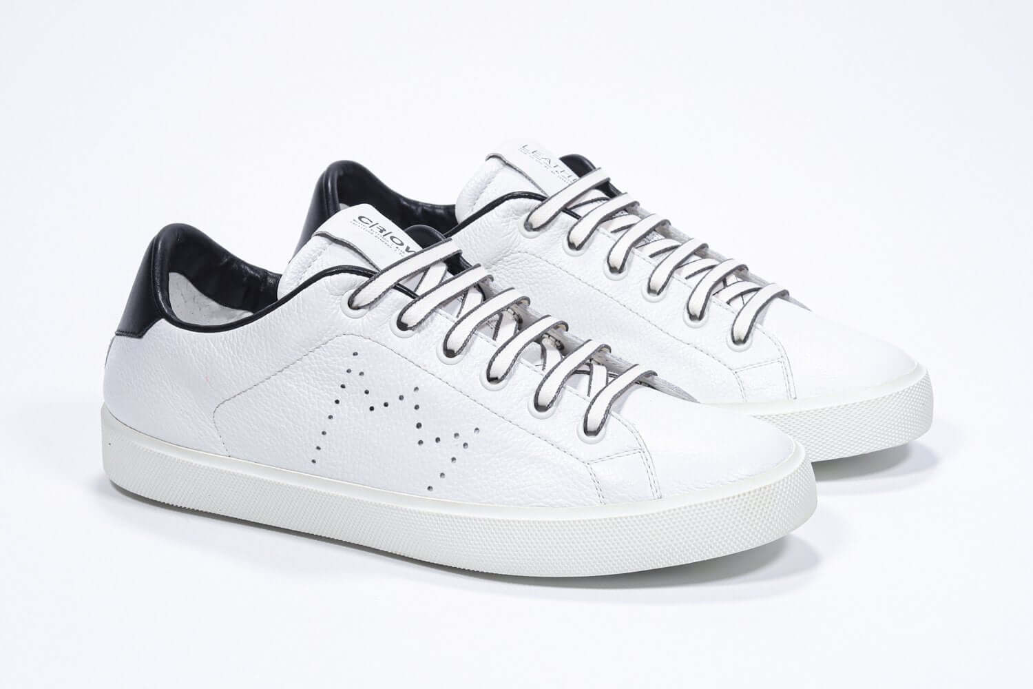 Three quarter view of low top white sneaker with black detailing and perforated crown logo on upper. Full leather upper and white rubber sole.