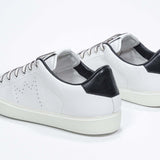 Three quarter back view of low top white sneaker with black detailing and perforated crown logo on upper. Full leather upper and white rubber sole.