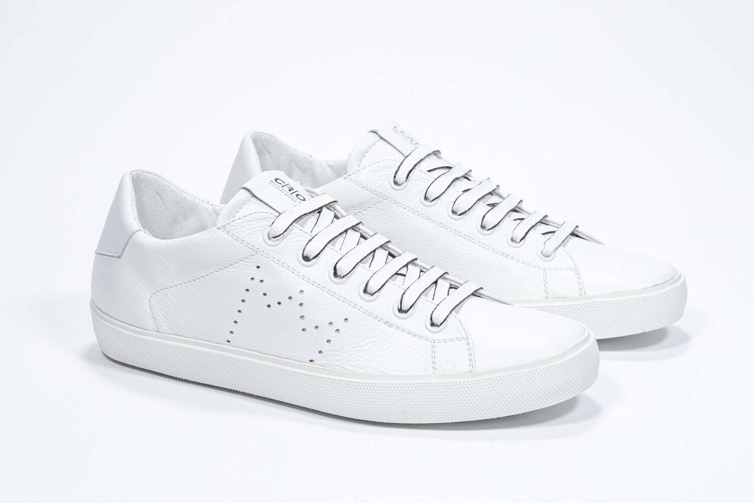 Three quarter front view of low top white sneaker with perforated crown logo on upper. Full leather upper and white rubber sole.