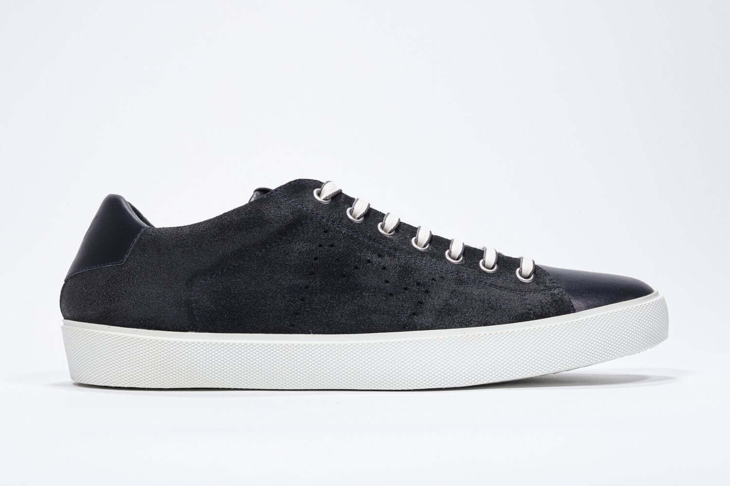 Side profile of low top navy sneaker with perforated crown logo on upper. Full suede upper and white rubber sole.