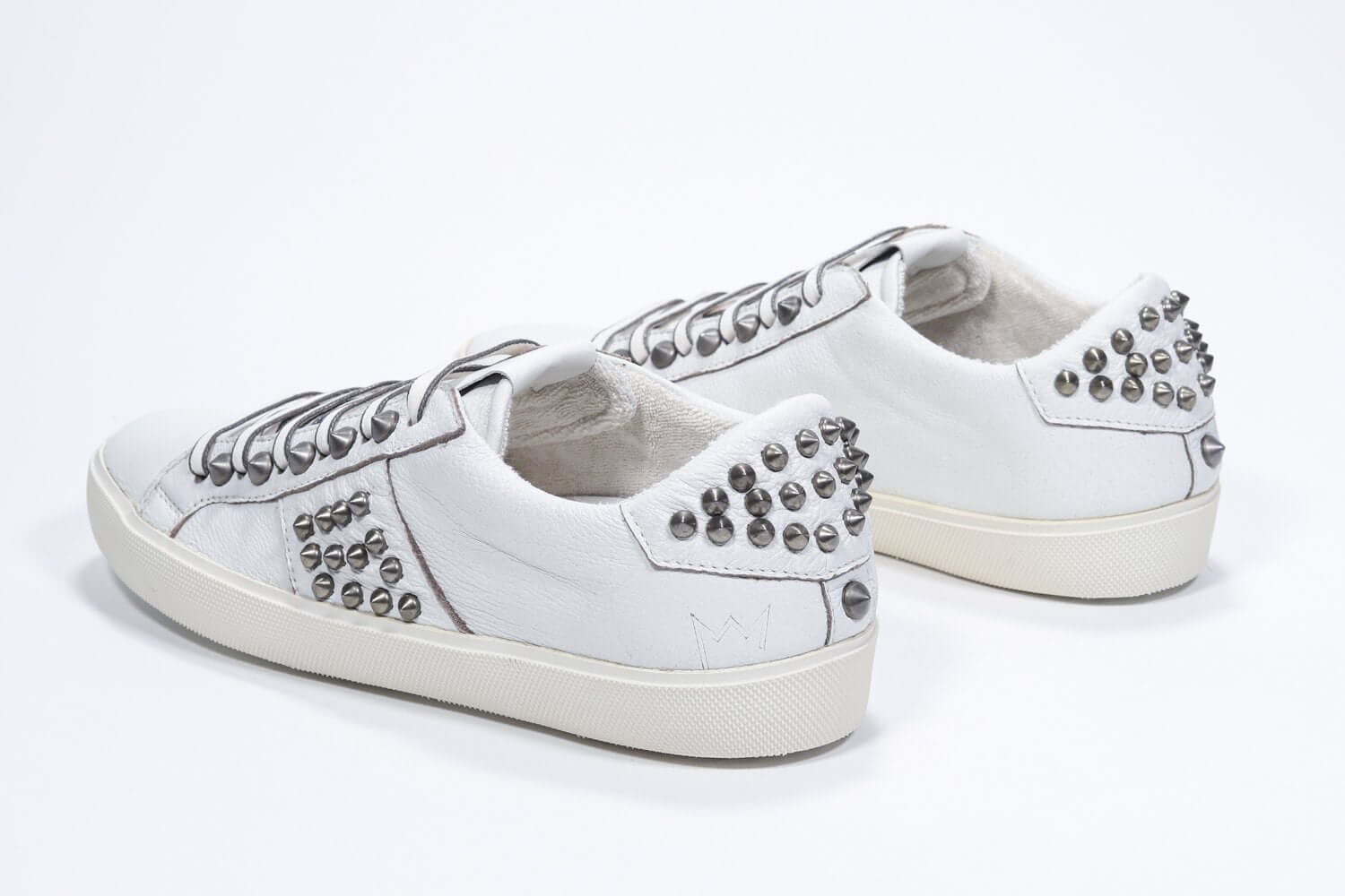 Three quarter back view of low top white sneaker. Full leather upper with studs and vintage rubber sole.