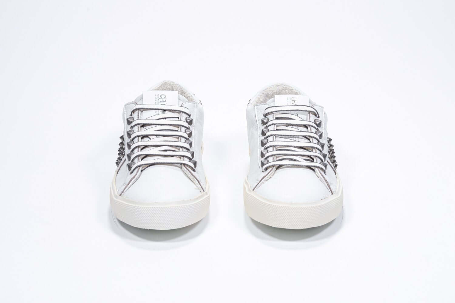 Front view of low top white sneaker. Full leather upper with studs and vintage rubber sole.