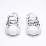 Front view of low top white sneaker. Full leather upper with studs and vintage rubber sole.