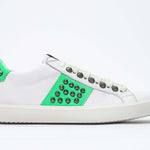Side profile of low top white and fluo green sneaker. Full grain leather upper with gun metal studs and white rubber sole.