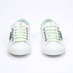 Front view of low top white and fluo green sneaker. Full grain leather upper with gun metal studs and white rubber sole.