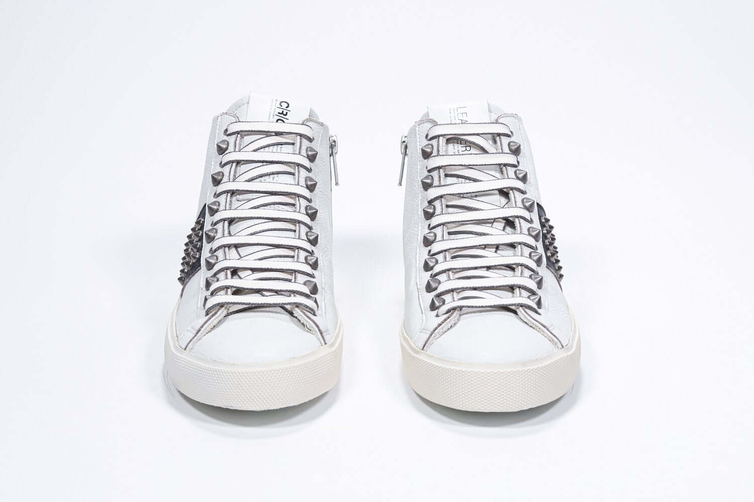 Front view of mid top white and black sneaker. Full leather upper with studs, an internal zip and vintage rubber sole.