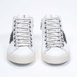 Front view of mid top white and navy sneaker. Full leather upper with studs, an internal zip and vintage rubber sole.