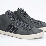 Three quarter front view of mid top military green sneaker. Suede and leather upper with studs, an internal zip and vintage rubber sole.