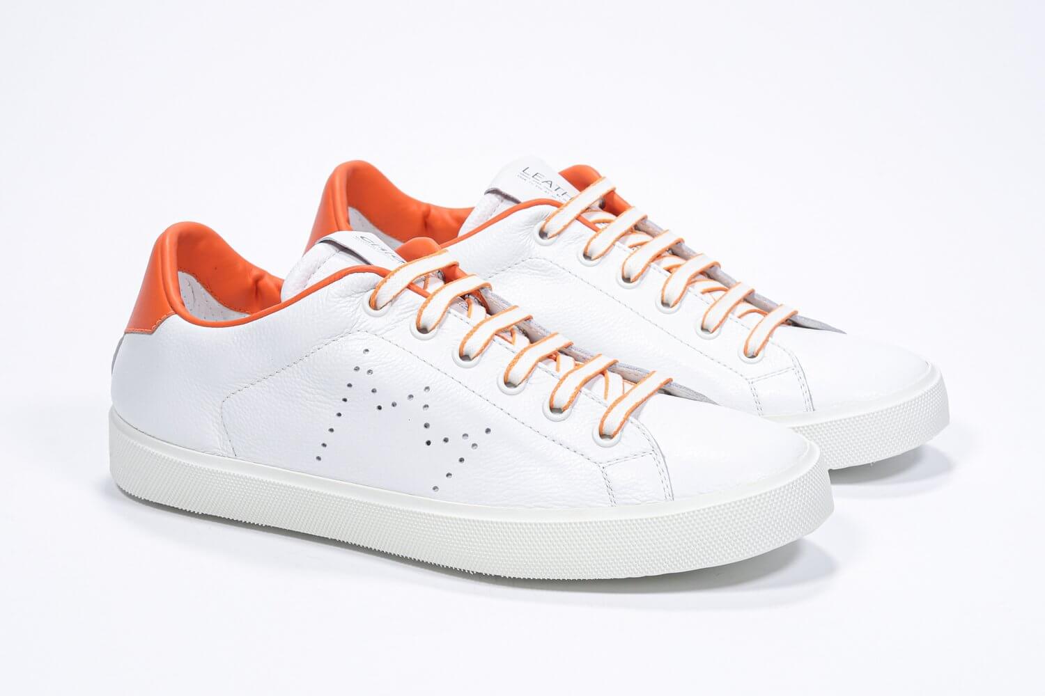 Three quarter front view of low top white sneaker with orange detailing and perforated crown logo on upper. Full leather upper and white rubber sole.
