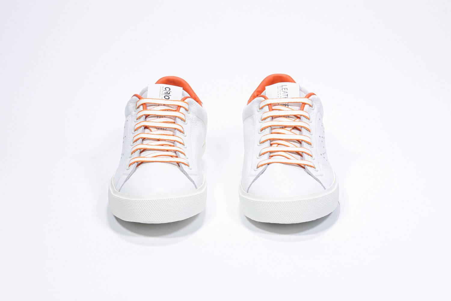Front view of low top white sneaker with orange detailing and perforated crown logo on upper. Full leather upper and white rubber sole.