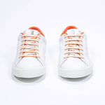 Front view of low top white sneaker with orange detailing and perforated crown logo on upper. Full leather upper and white rubber sole.