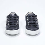 Front view of low top black sneaker. Full leather upper with studs and white rubber sole.