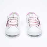 Front view of low top white and neon pink sneaker. Full leather upper with studs and white rubber sole.