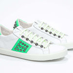 Three quarter front view of low top white and neon green sneaker. Full leather upper with studs and white rubber sole.