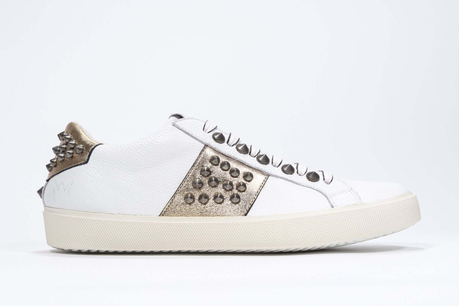 Side profile of low top white and metallic gold sneaker. Full leather upper with studs and vintage rubber sole.