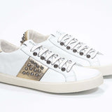 Three quarter front view of low top white and metallic gold sneaker. Full leather upper with studs and vintage rubber sole.