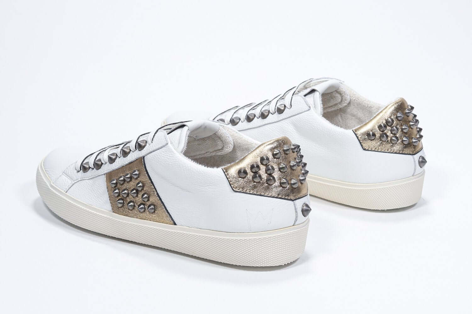 Three quarter back view of low top white and metallic gold sneaker. Full leather upper with studs and vintage rubber sole.