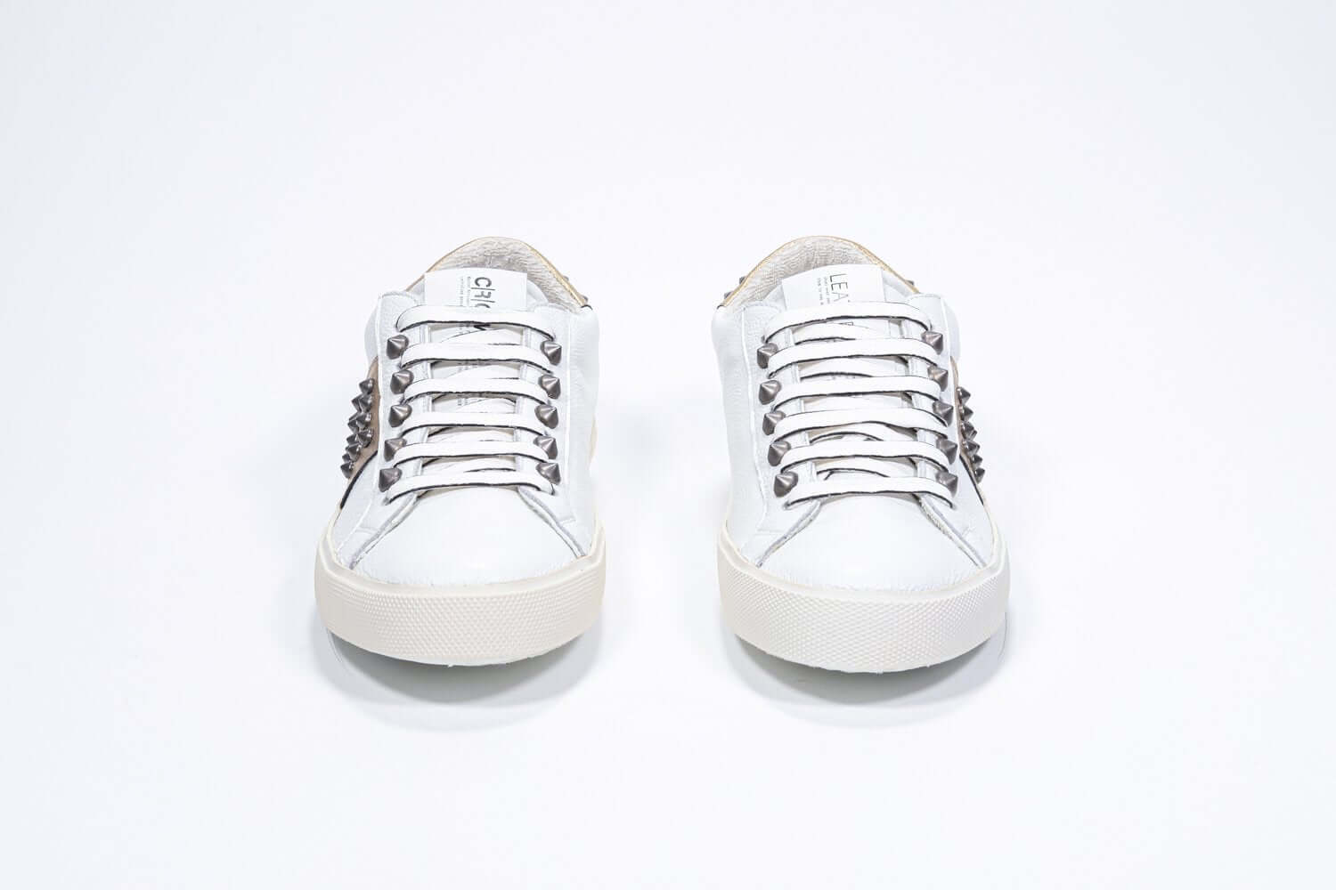 Front view of low top white and metallic gold sneaker. Full leather upper with studs and vintage rubber sole.