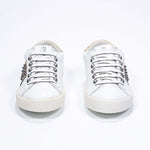Front view of low top white and metallic gold sneaker. Full leather upper with studs and vintage rubber sole.