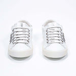Front view of low top white and metallic silver sneaker. Full leather upper with studs and vintage rubber sole.