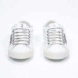Front view of low top white and metallic silver sneaker. Full leather upper with studs and vintage rubber sole.