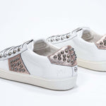 Three quarter back view of low top white and metallic rose sneaker. Full leather upper with studs and vintage rubber sole.