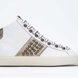 Side profile of mid top white and metallic gold sneaker. Full leather upper with studs, an internal zip and vintage rubber sole.
