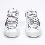Front view of mid top white and metallic gold sneaker. Full leather upper with studs, an internal zip and vintage rubber sole.