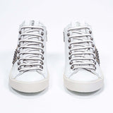 Front view of mid top white and metallic gold sneaker. Full leather upper with studs, an internal zip and vintage rubber sole.